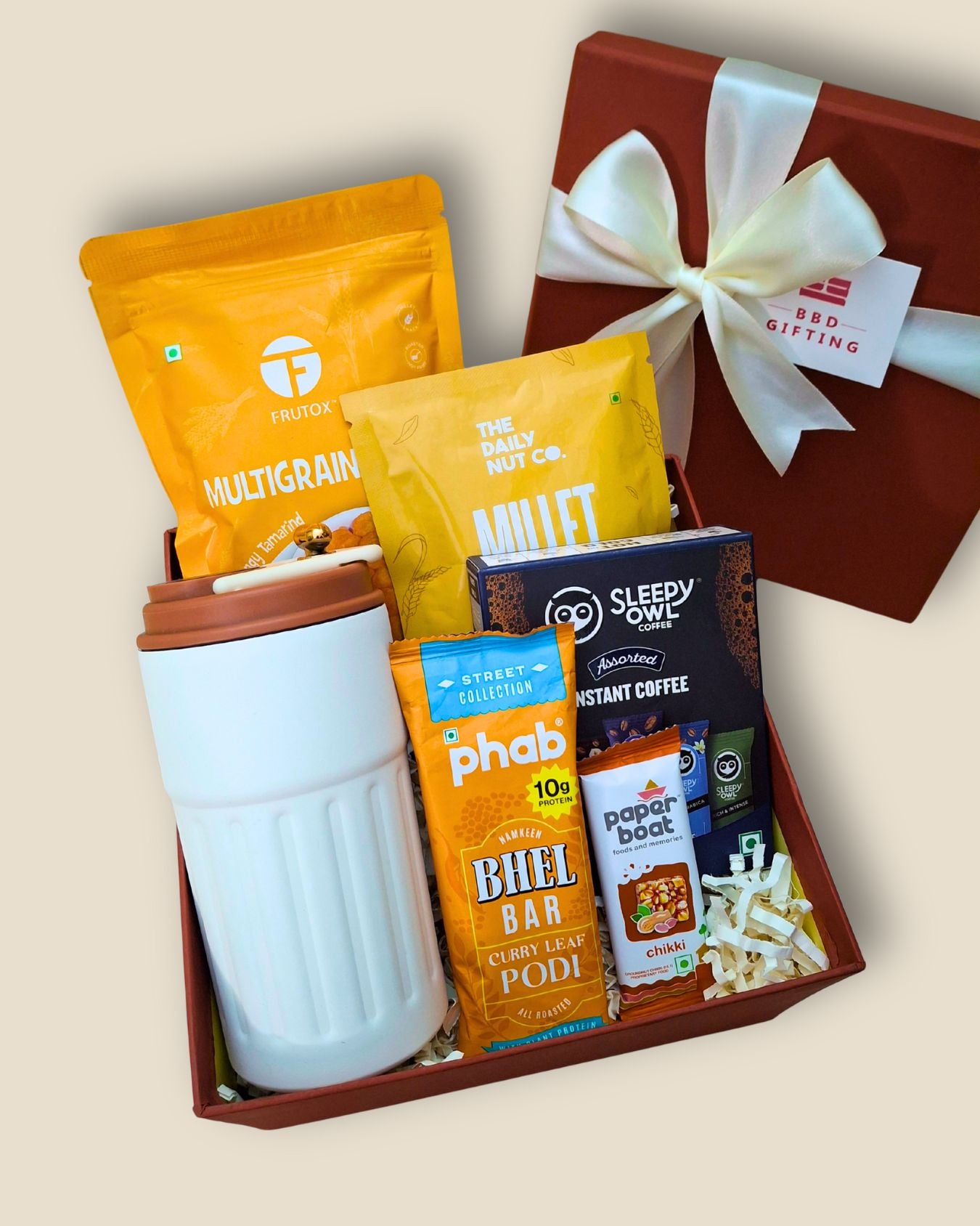 Gift basket with snacks, a tumbler, and a box labeled 'BBD Gifting' on a beige background.