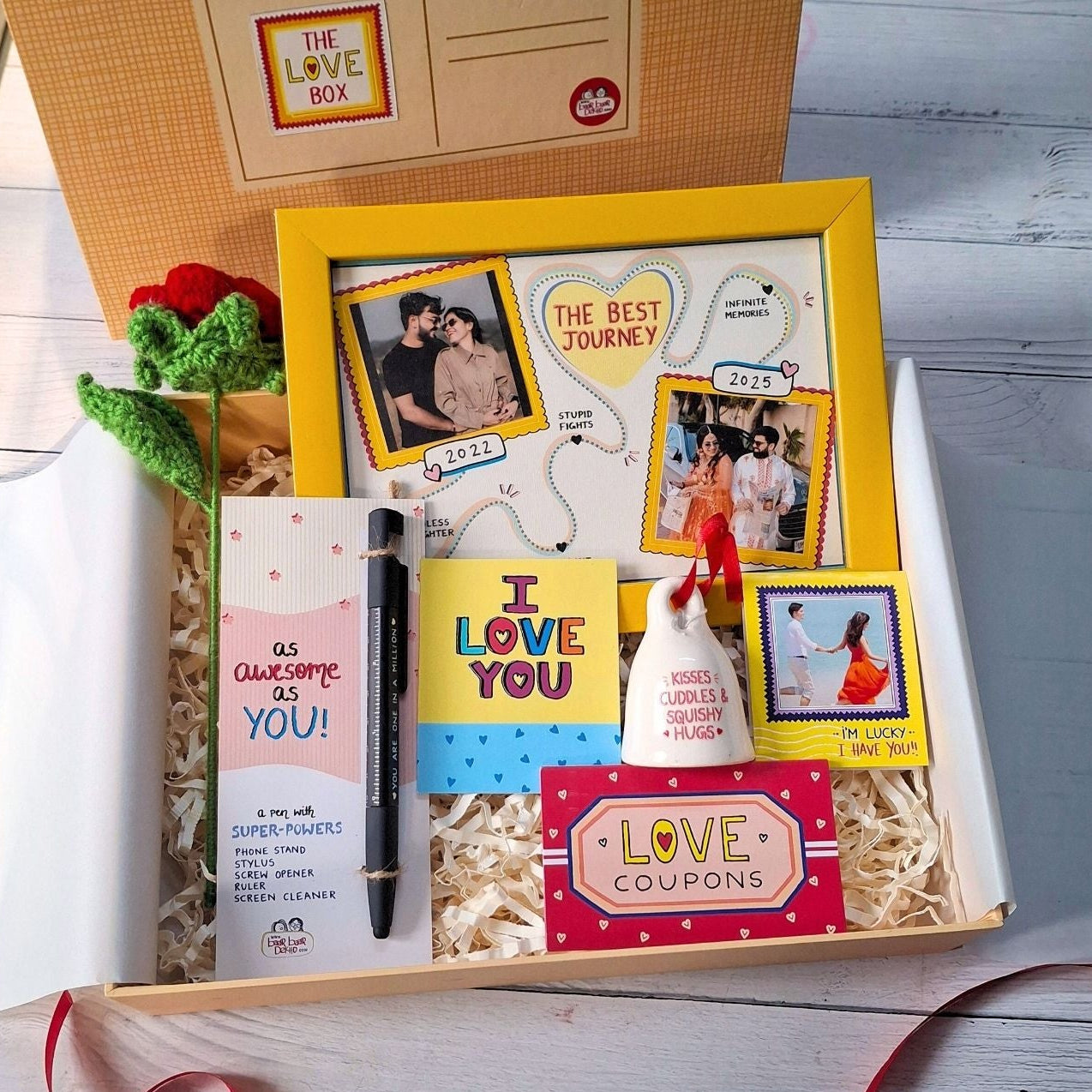 Gift box with various items including a mug, photos, and a card on a wooden surface.