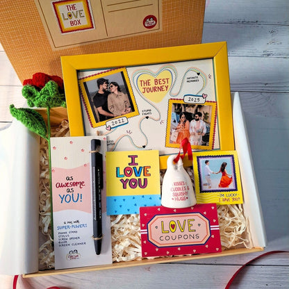 Love-themed gift box with photos, cards, and stationery on a wooden surface