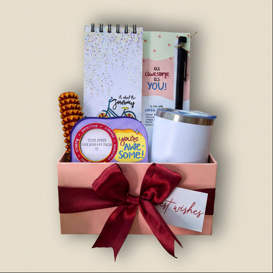 Gift set with a notebook, pen, tumbler, and other items arranged in a box with a red ribbon on a beige background.