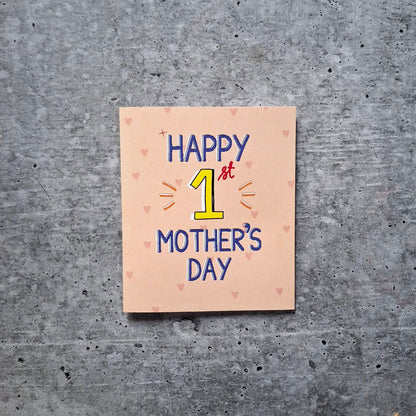 Card with 'Happy 1st Mother's Day' text on a textured gray surface